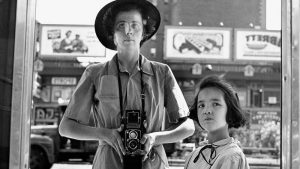 تصویر عکس خاکستری از سلف پرتره ویویان مایر که در کنار او دختر بچه‌ای ایستاده