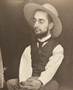 تولوز لوترک تصویر عکس خاکستری که تولوز لوترک نشسته بر چهارپایه و کلاهی به سر دارد